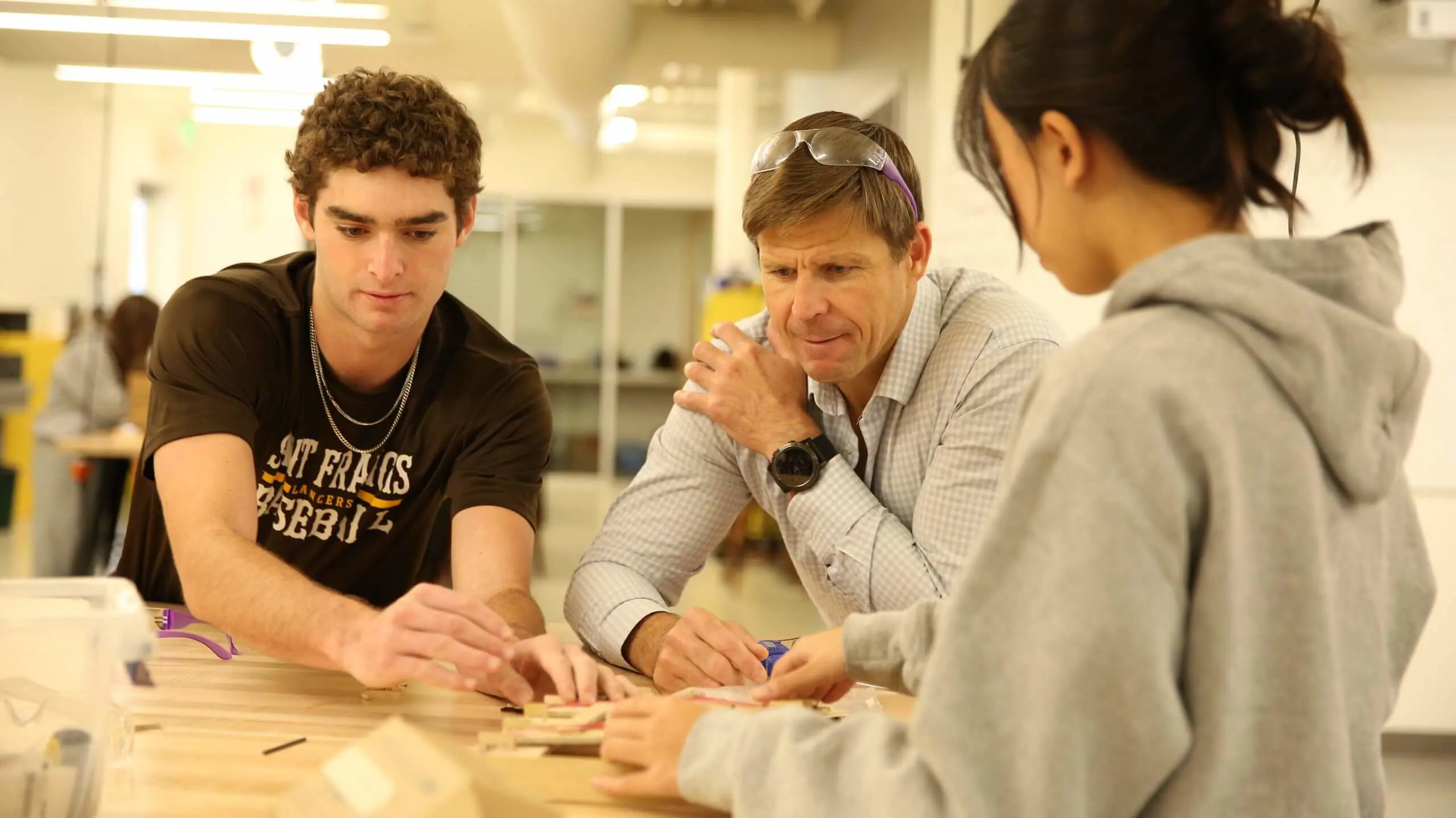 An educator and two students collaborate over a wooden puzzle at a table in a bright classroom. The atmosphere is focused and engaged.