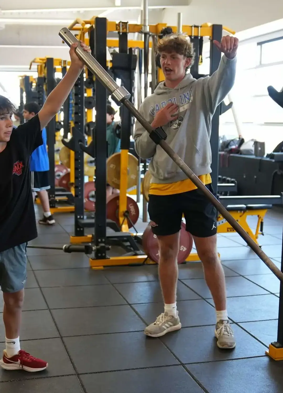 A camp counselor helping a camper exercise with a dumbbell in the weight room.