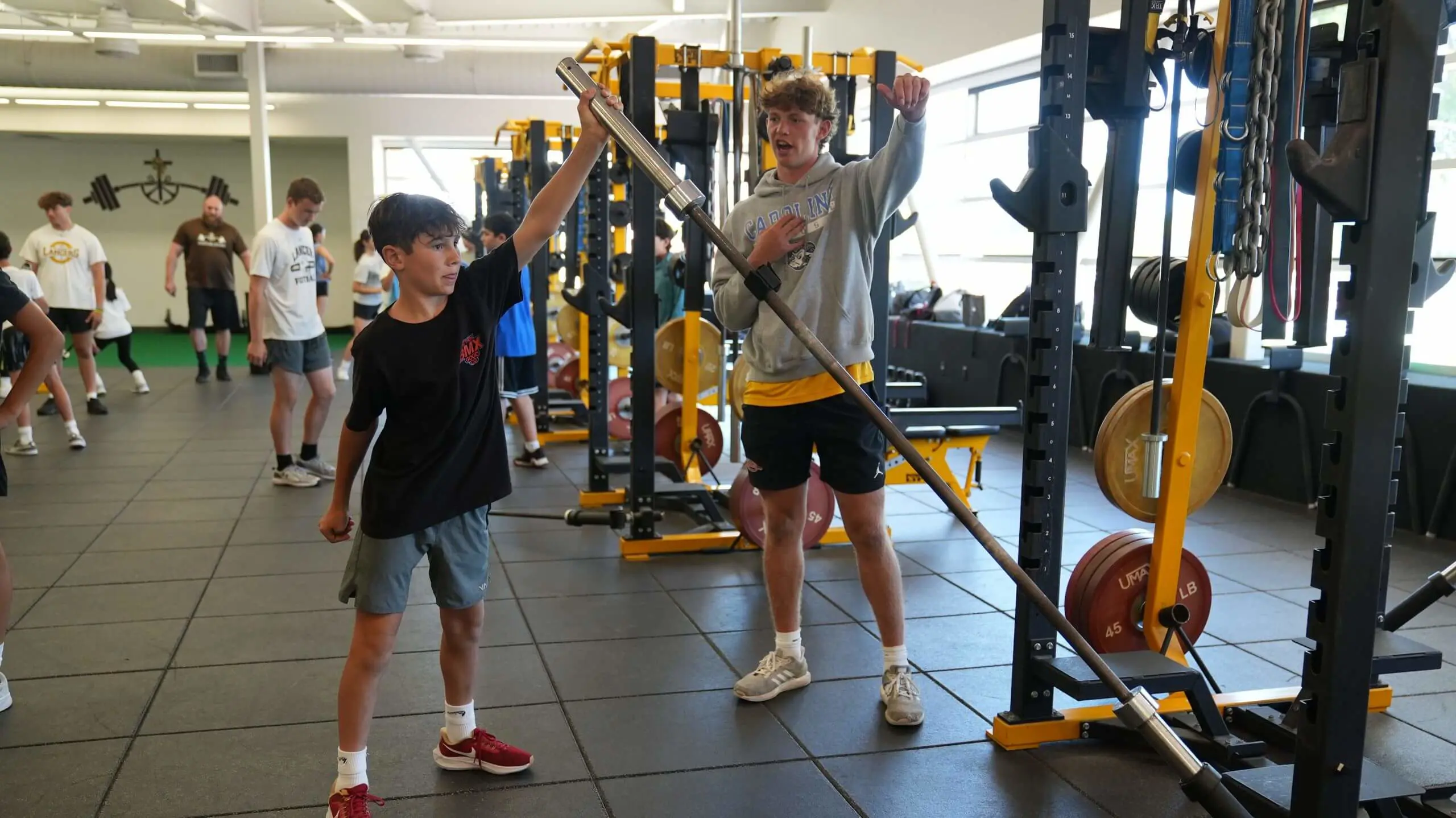 A camp counselor helping a camper exercise with a dumbbell in the weight room.