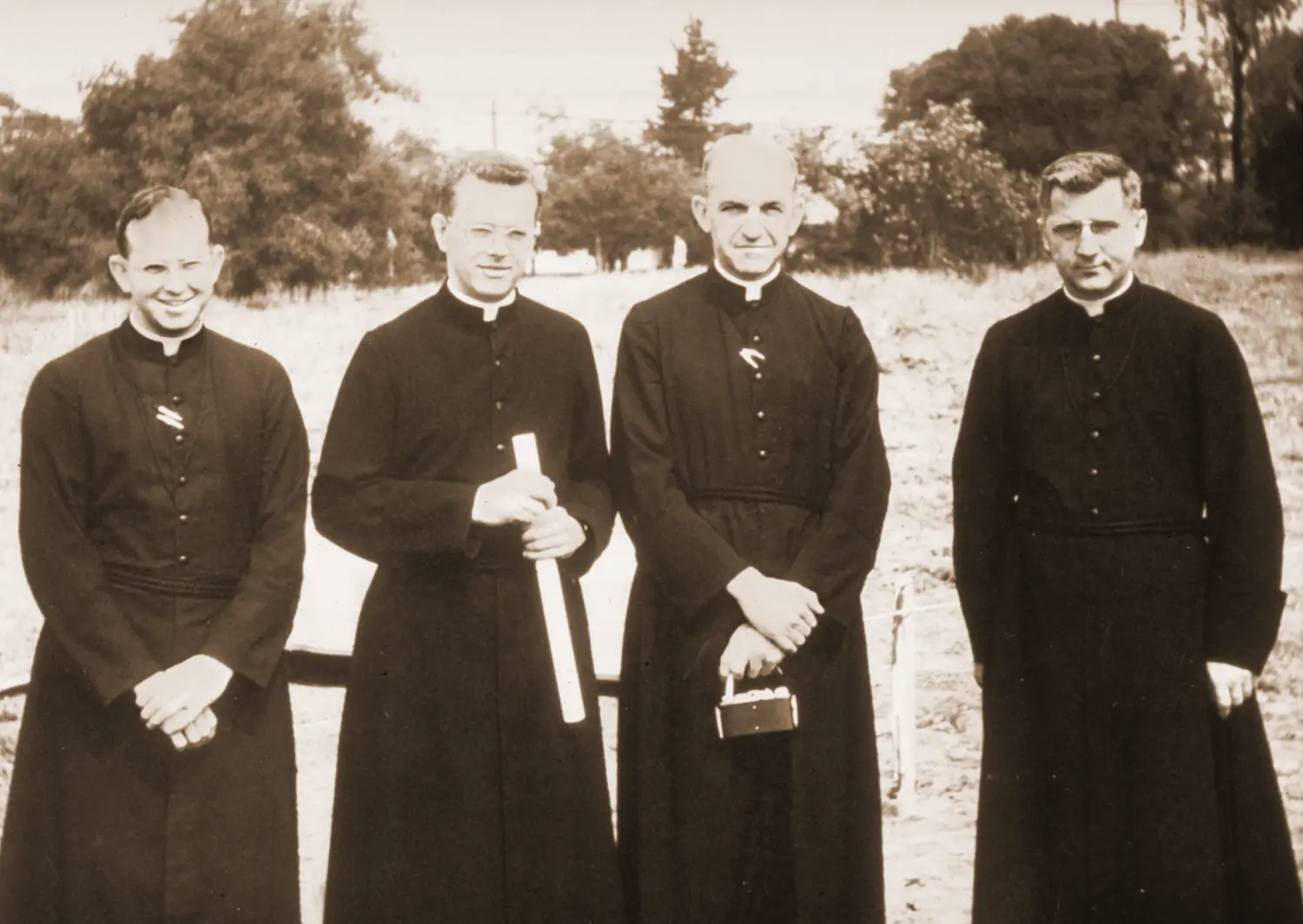 Brothers posing for a picture on the land that will become the campus with the designs for the original school in hand.