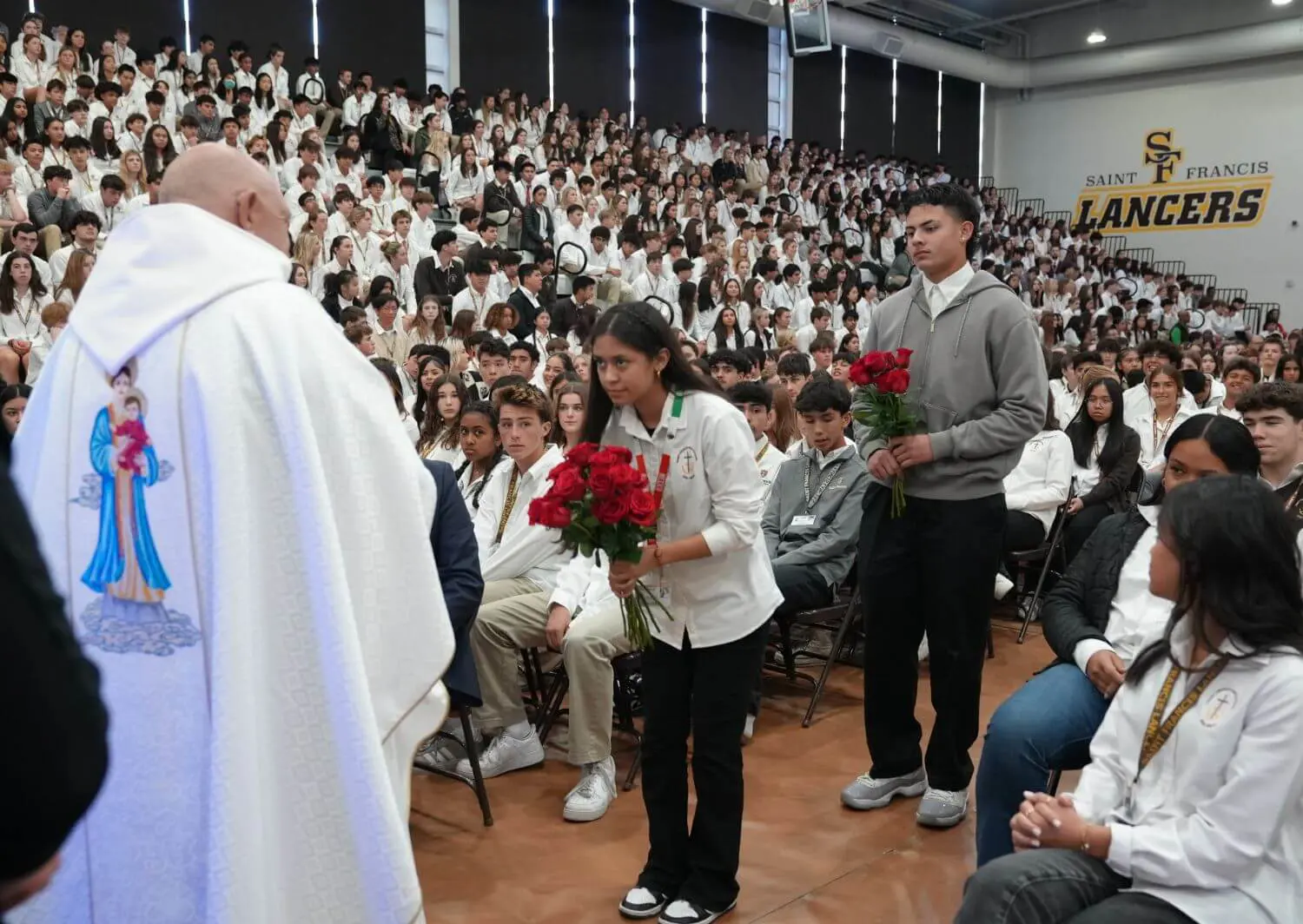 Students in a packed Saint Francis High School gymnasium present bouquets of red roses to Father Tony Mancuso during a religious ceremony honoring Our Lady of Guadalupe.