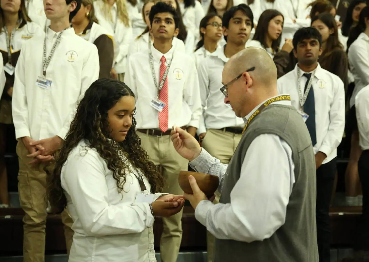 An educator serving as eucharistic minister at mass, while student receives communion.