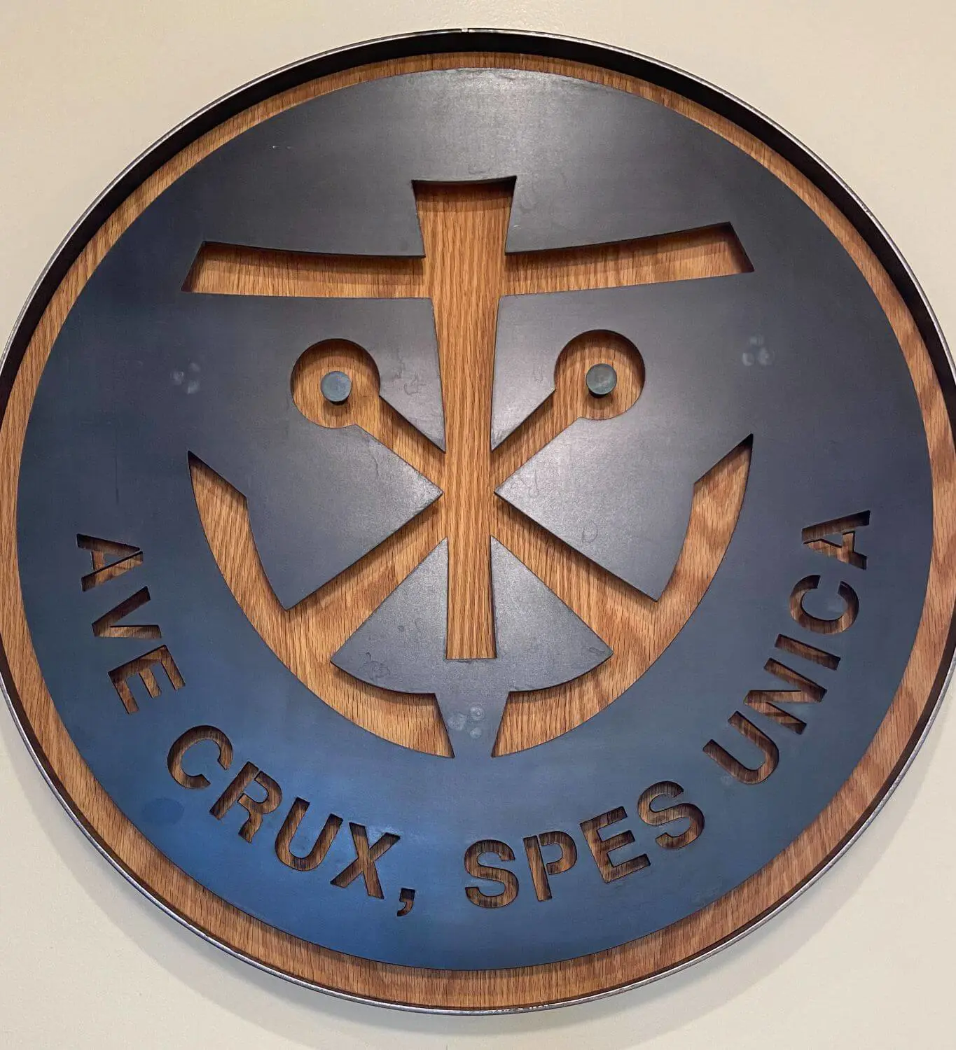 A circular wooden and metal wall hanging features the Holy Cross symbol with the Latin phrase "Ave Crux, Spes Unica," meaning "Hail the Cross, Our Only Hope."