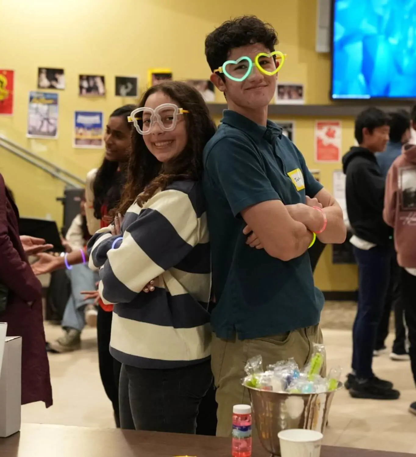 Students participating in a program standing back to back smiling with heart shaped glasses on.