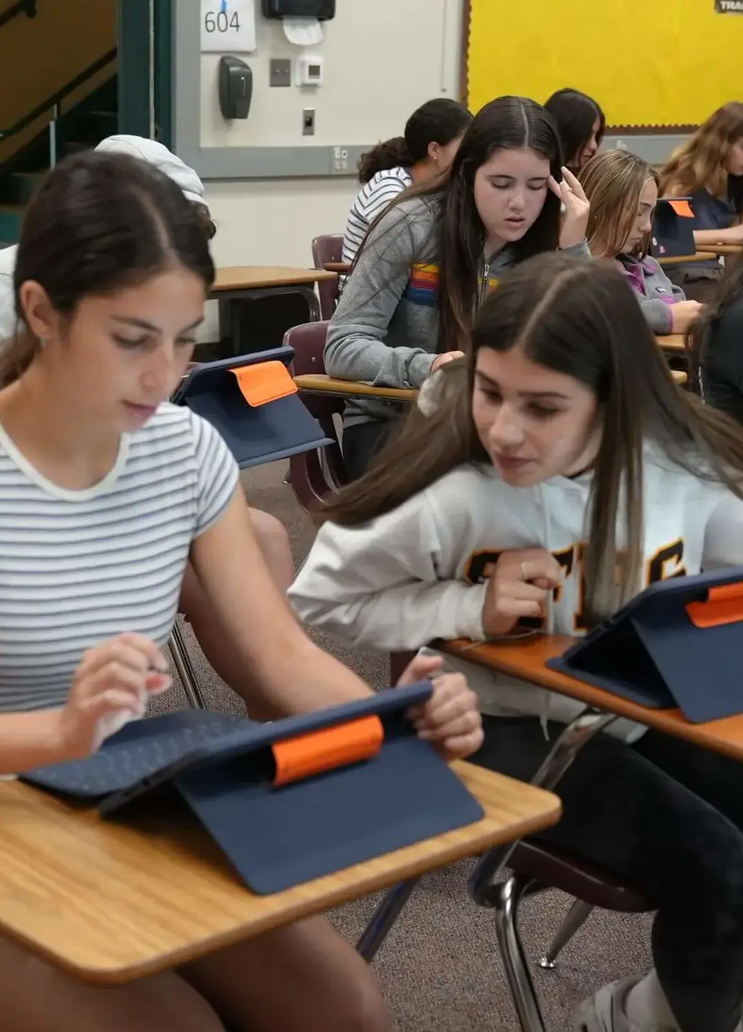 Two students seated in desks working on their iPads.