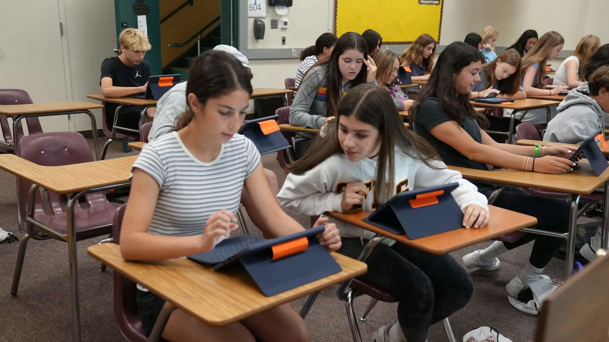 Two students seated in desks working on their iPads.