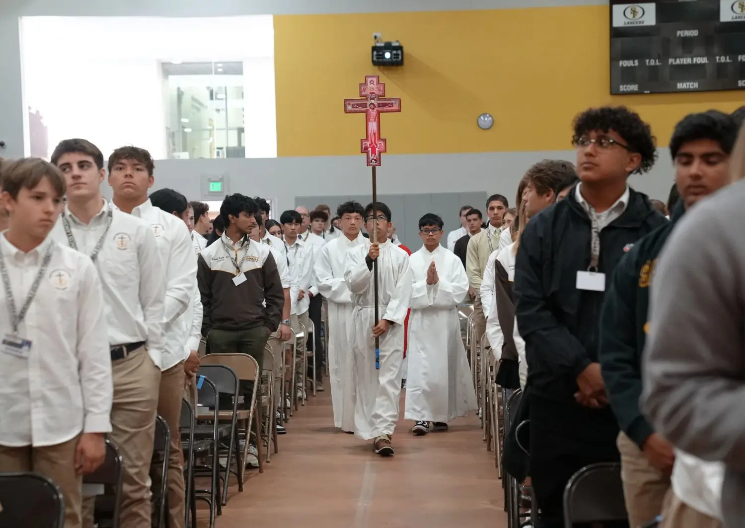Students approaching the altar during a mass entrance procession carrying a San Dominican cross.
