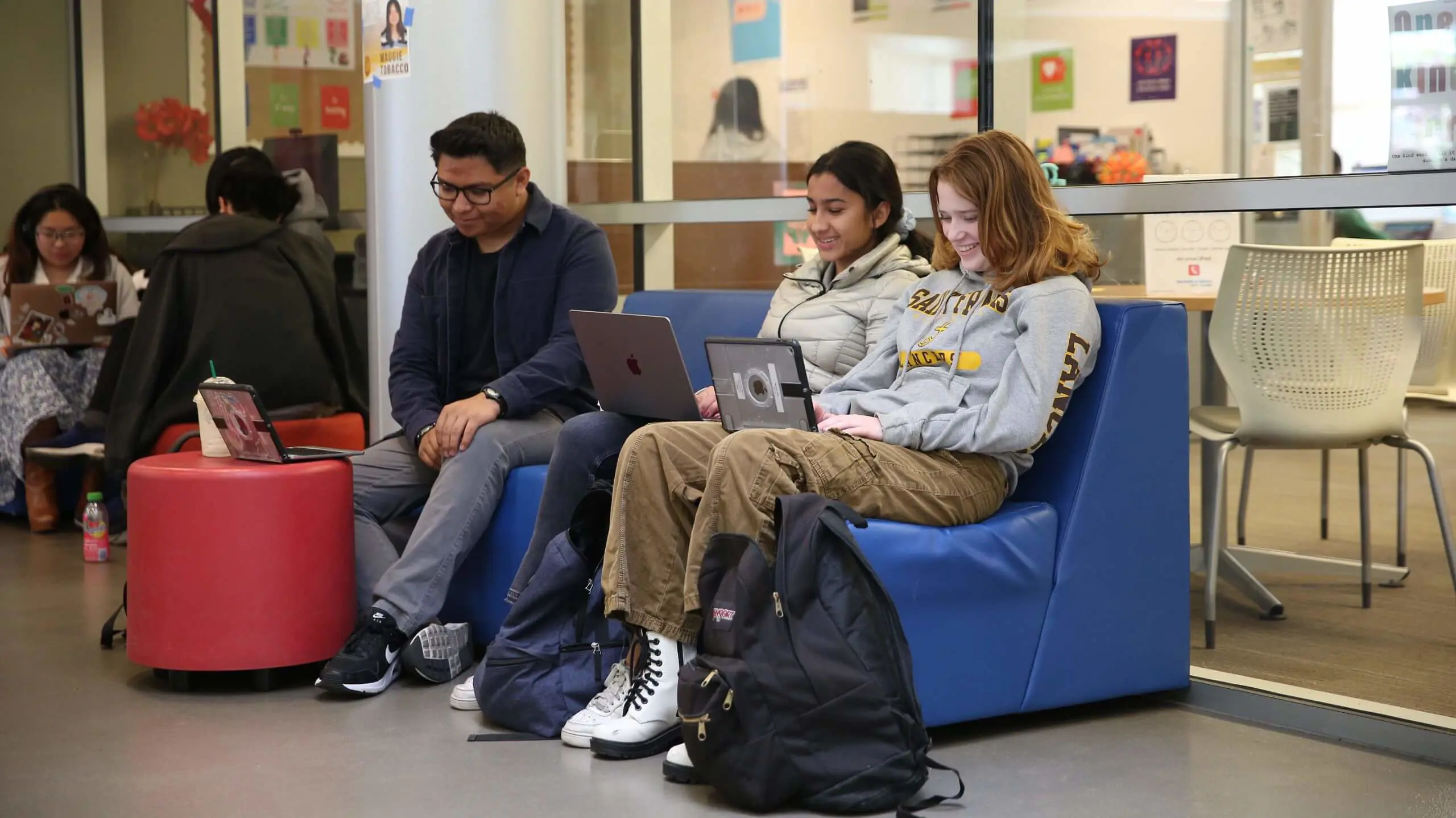 Two smiling Saint Francis students, sitting on a couch together working from their laptops.