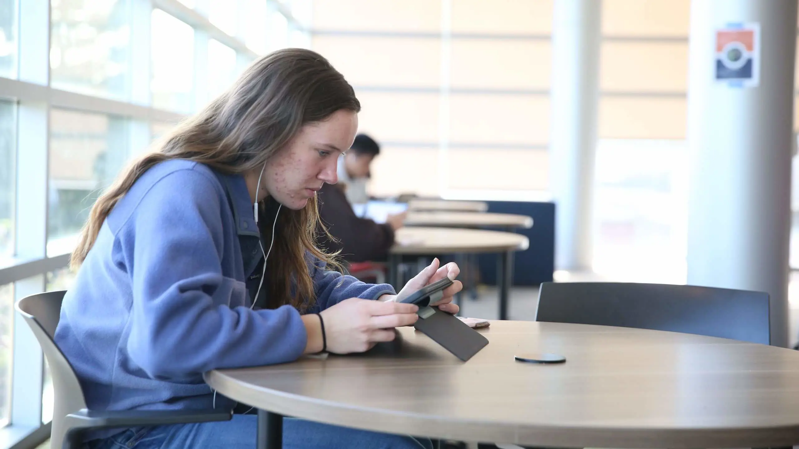 A student sitting at a table doing work on a tablet device.