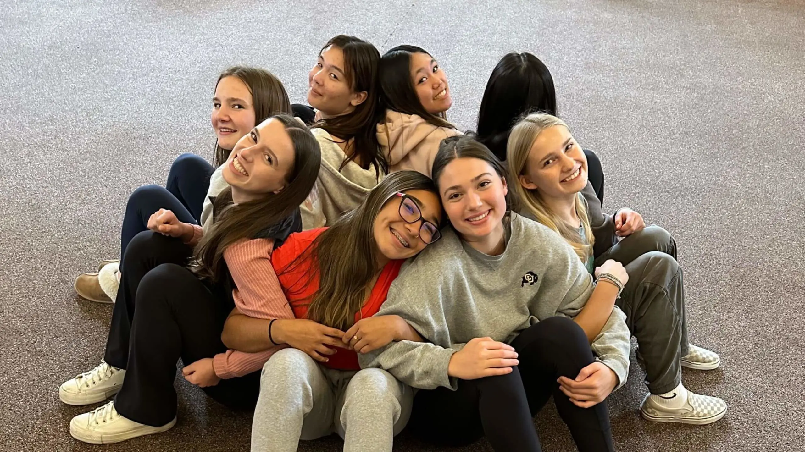 Students huddled together with their arms locked together happily smiling.