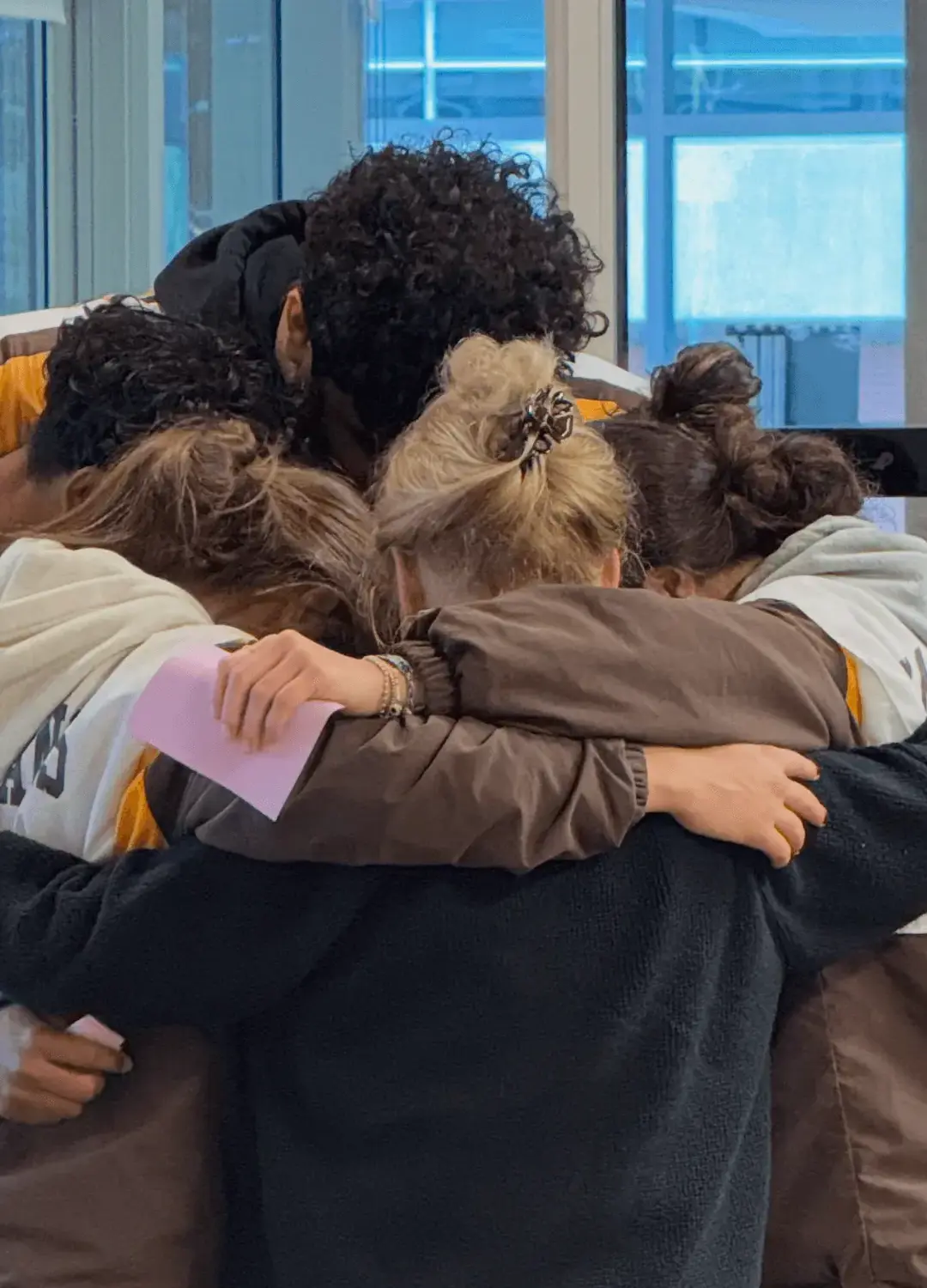 A group of students stand hugging each other with their adult retreat leader. 
