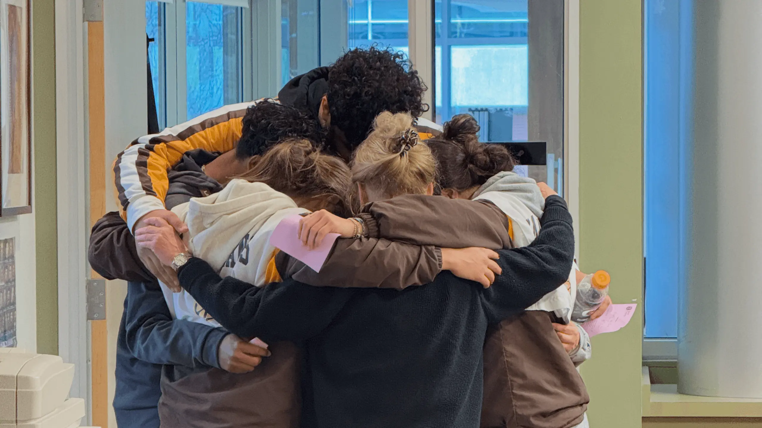 A group of students stand hugging each other with their adult retreat leader.