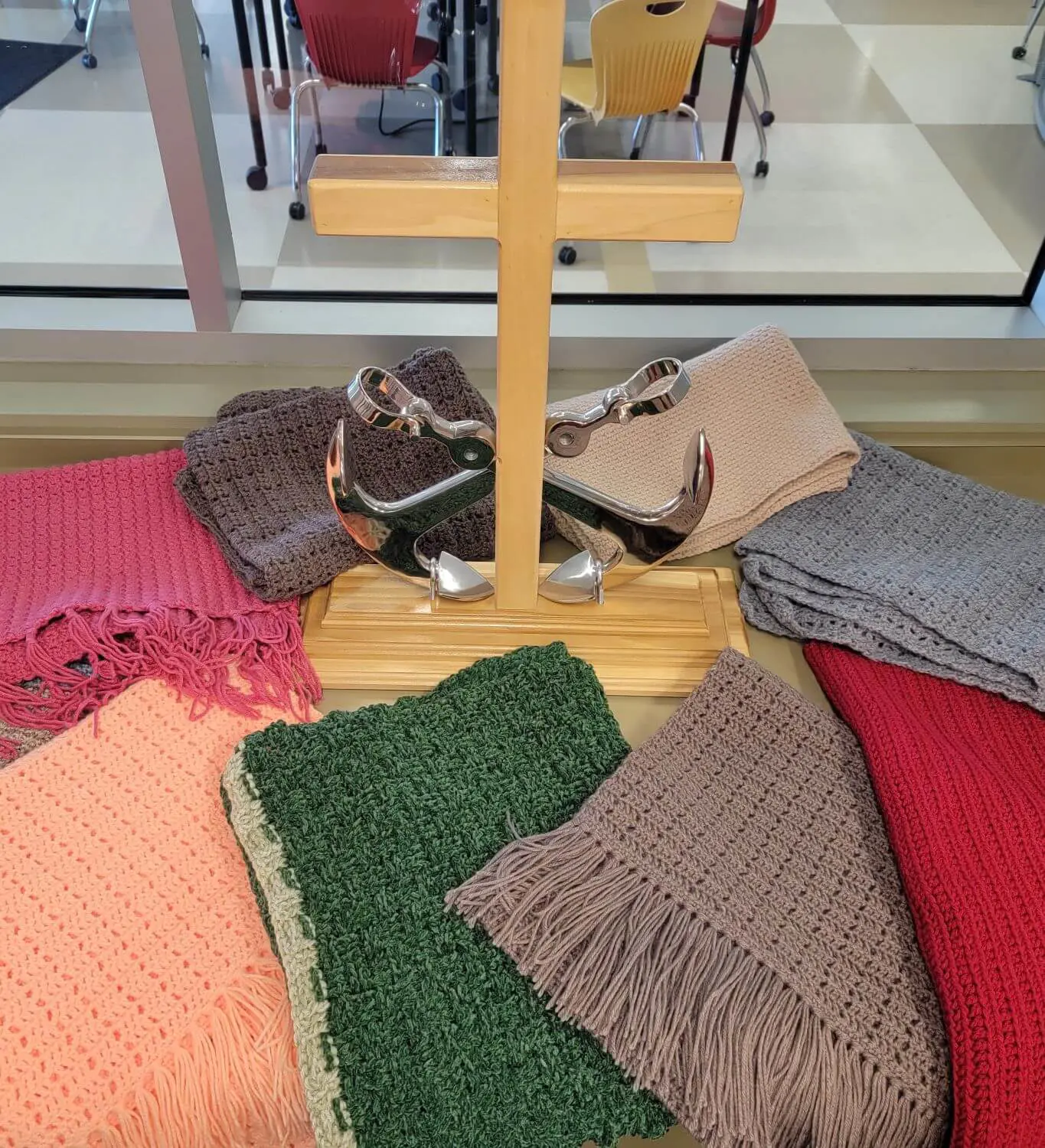 A wooden cross is displayed on a table with an assortment of colorful, handmade prayer blankets neatly arranged around it.