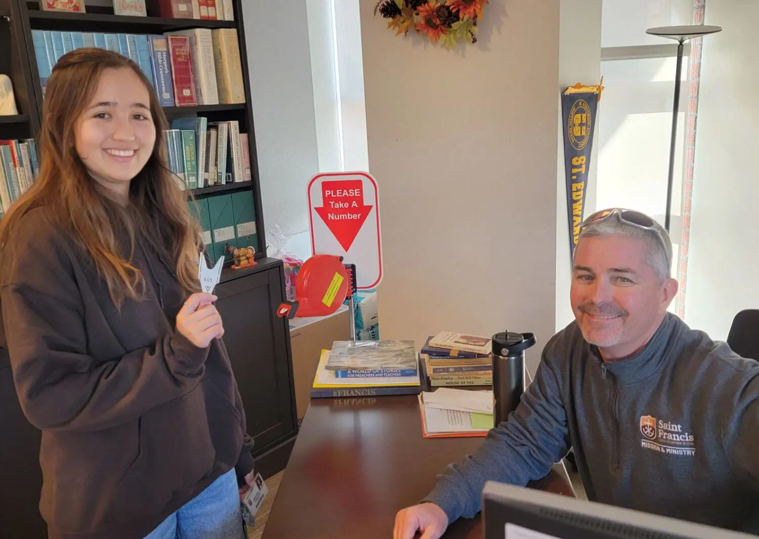 A female student stands at the desk of Campus Ministry Associate Dan Quinn.