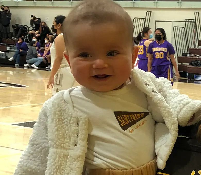 A baby sits in a chair, holding a stuffed animal, with a joyful expression on their face