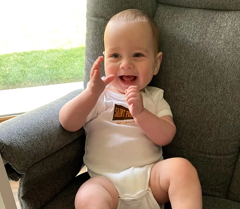 A baby sits in a chair, holding a stuffed animal, with a joyful expression on their face