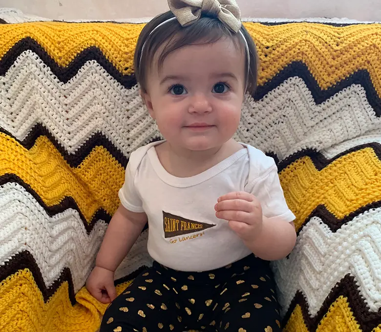  A baby girl is seated on a blanket featuring a yellow and black chevron design