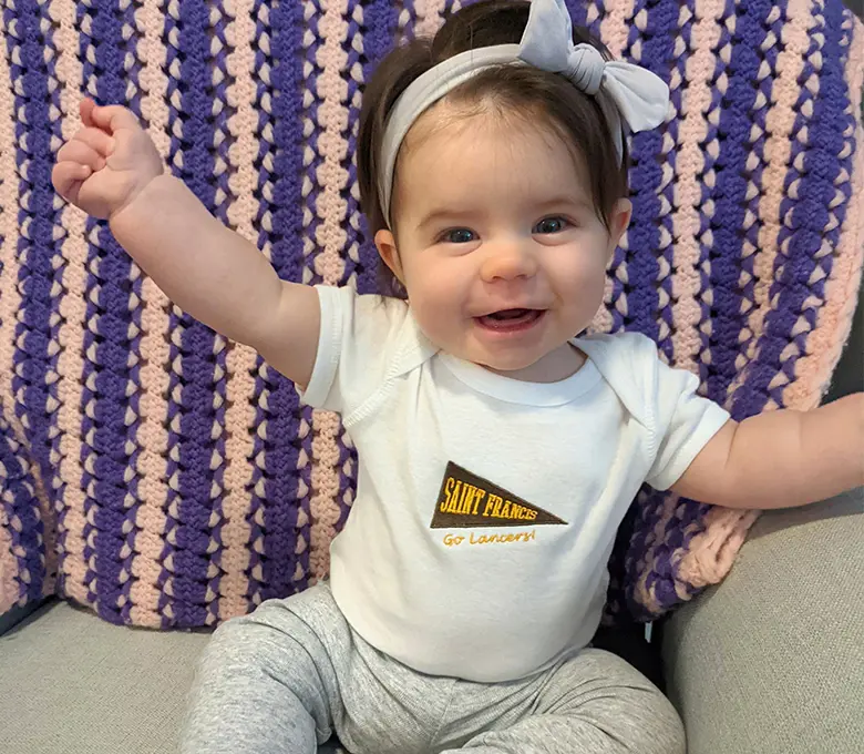 A baby sits in a chair, holding a stuffed animal, with a joyful expression on their face