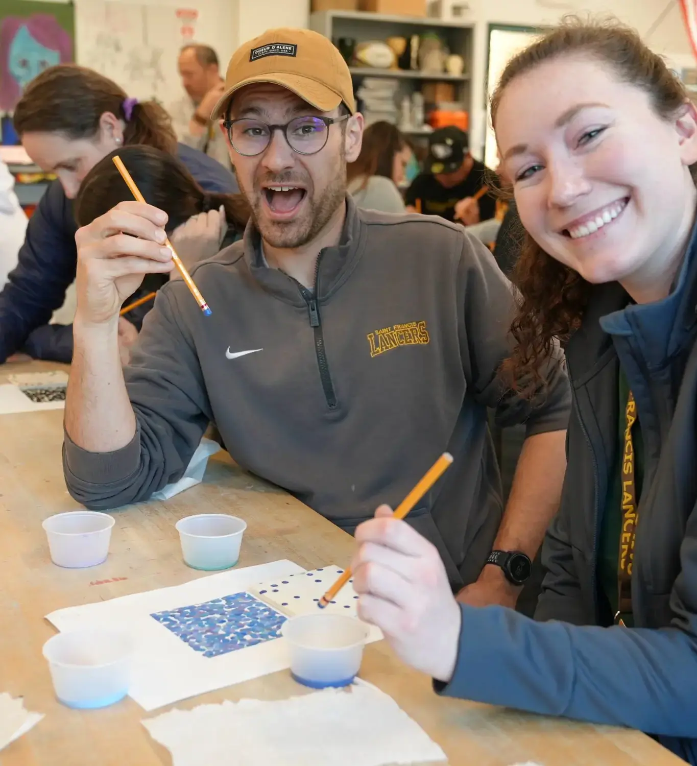 Educators happily painting at a table, each holding a paintbrush, surrounded by colorful art supplies