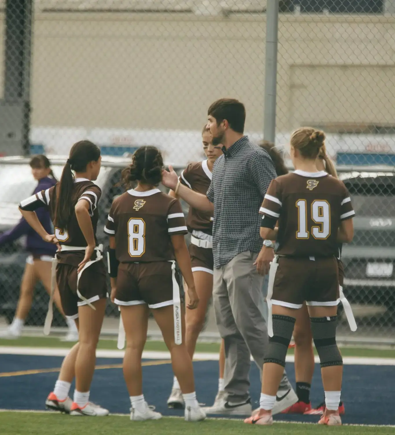 A coach stands with a group of girls in uniforms on a field, showcasing teamwork and camaraderie in sports