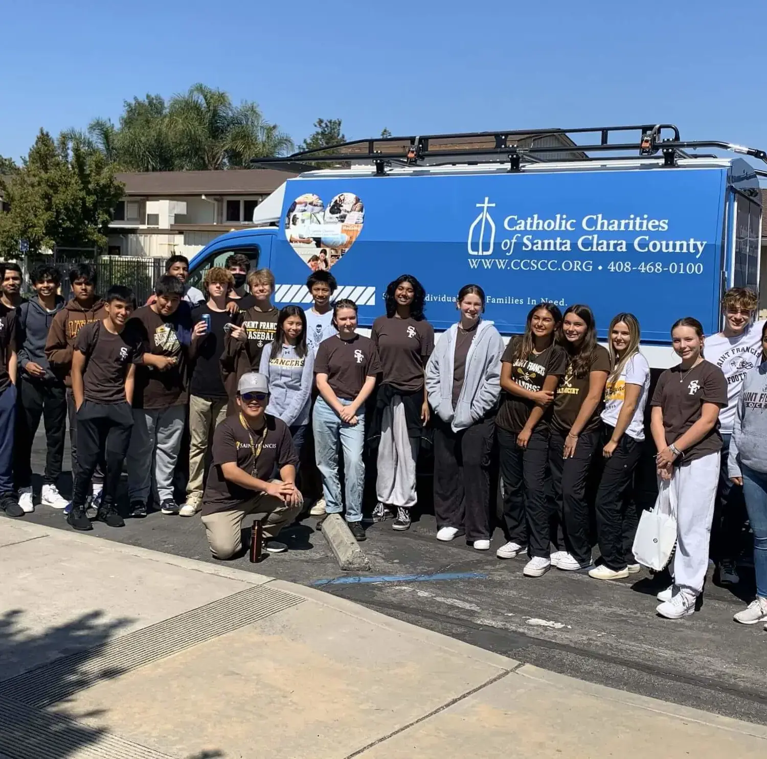 Students pose for a picture in front of a Catholic Charities van.