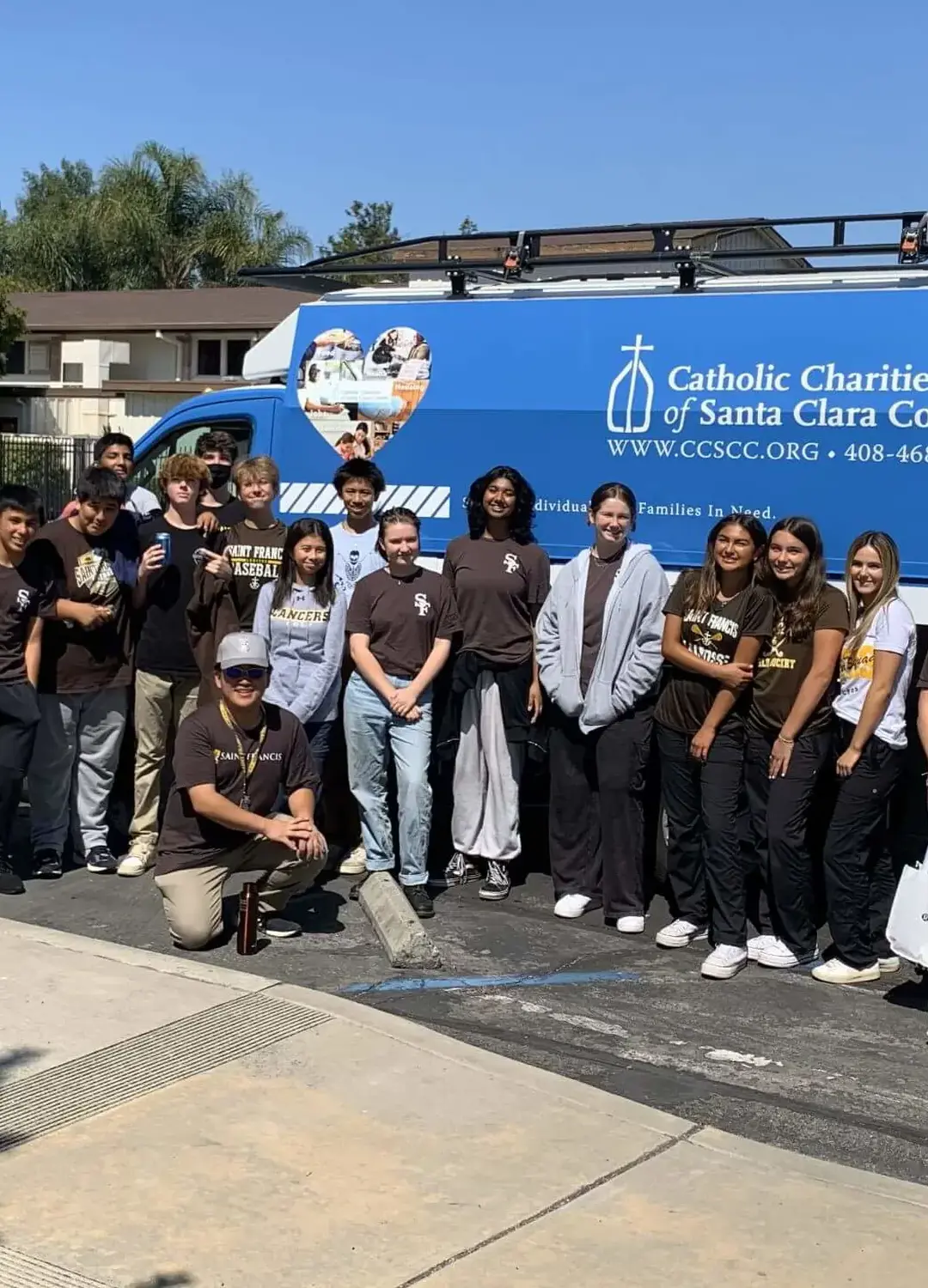 Students pose for a picture in front of a Catholic Charities van.