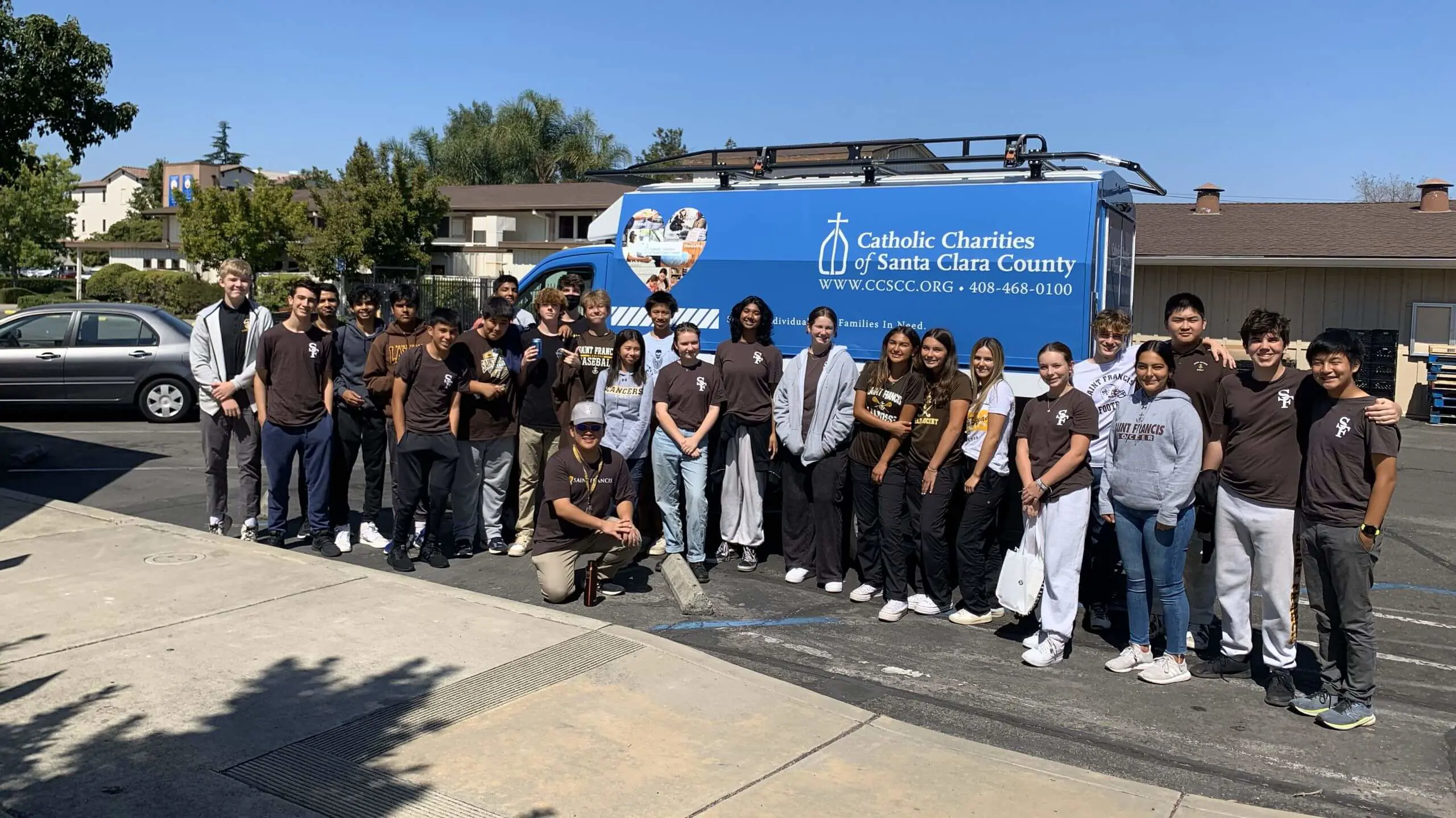 Students pose for a picture in front of a Catholic Charities van.