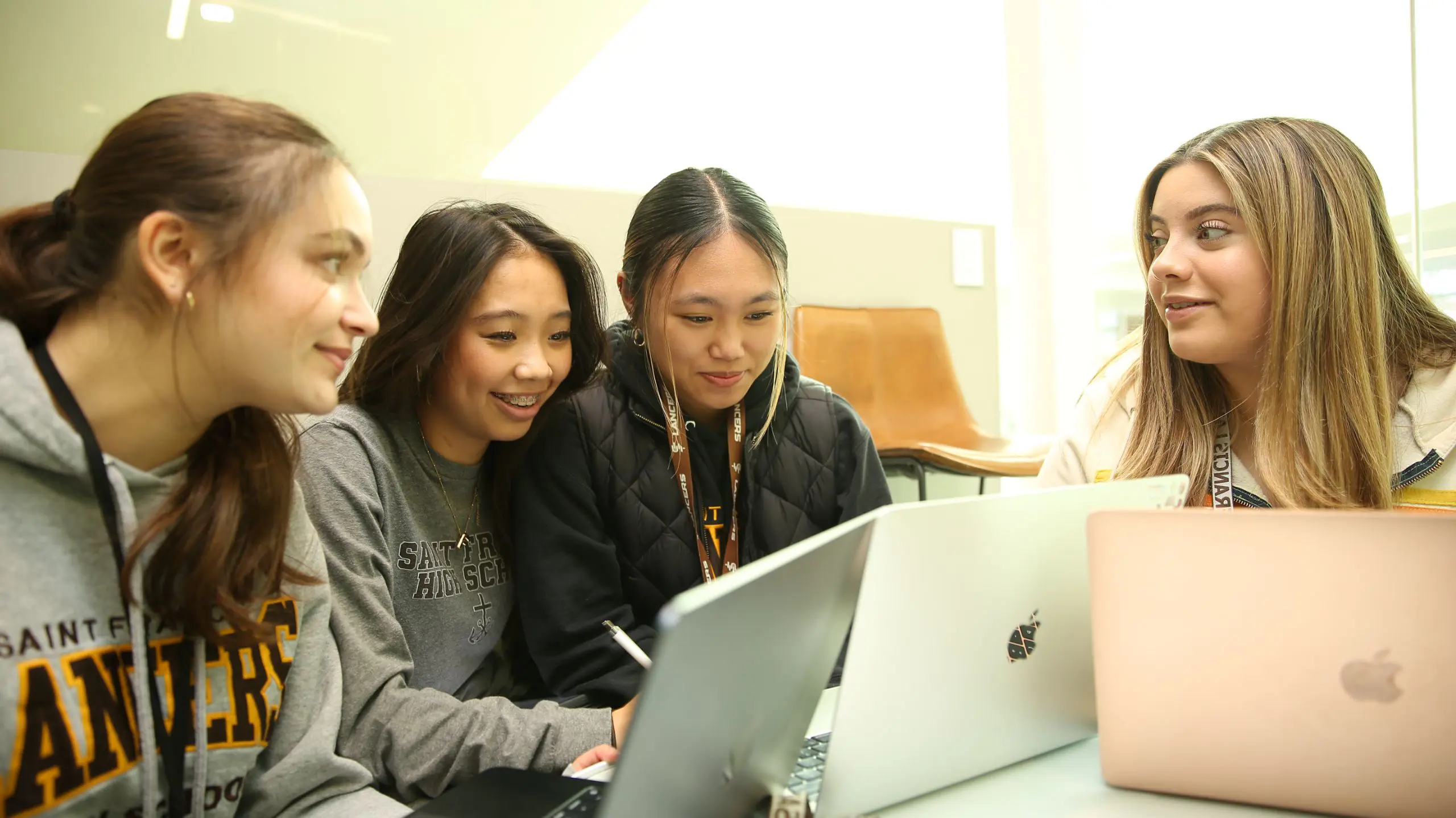 A group of students sitting together, looking at a laptop screen with curiosity and interest.
