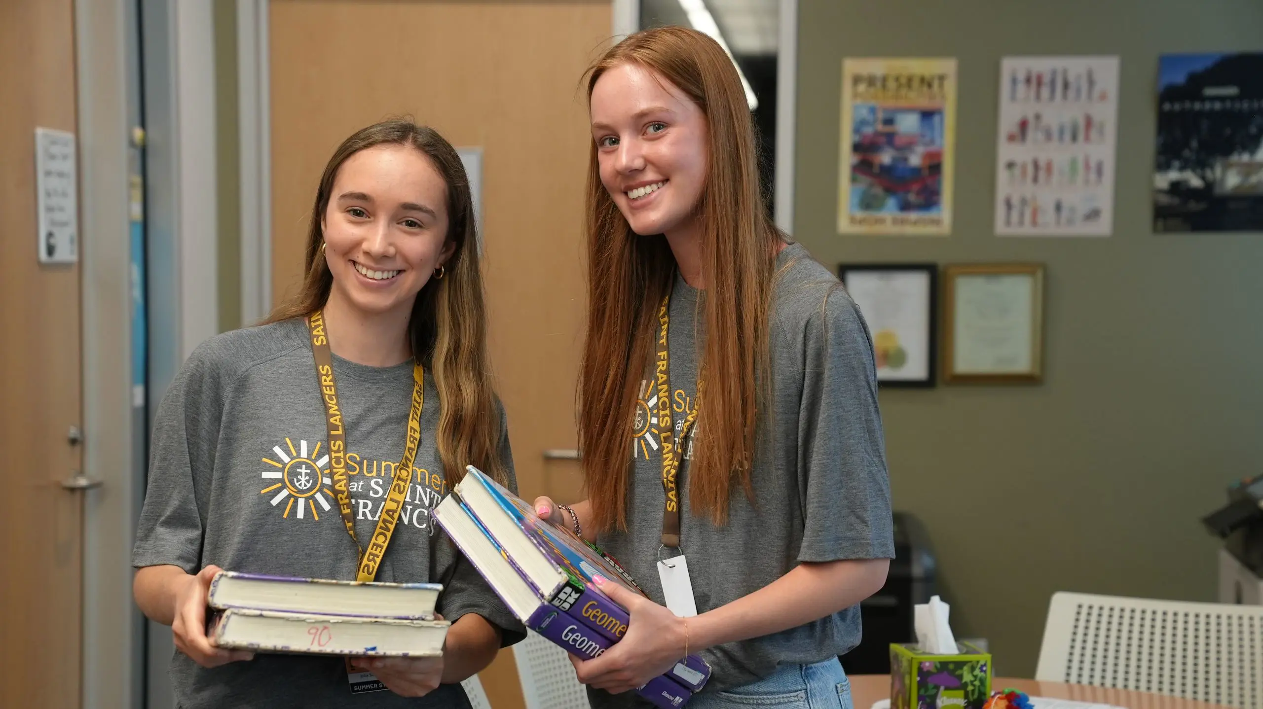 Two smiling Summer at Saint Francis teacher assistants holding books.