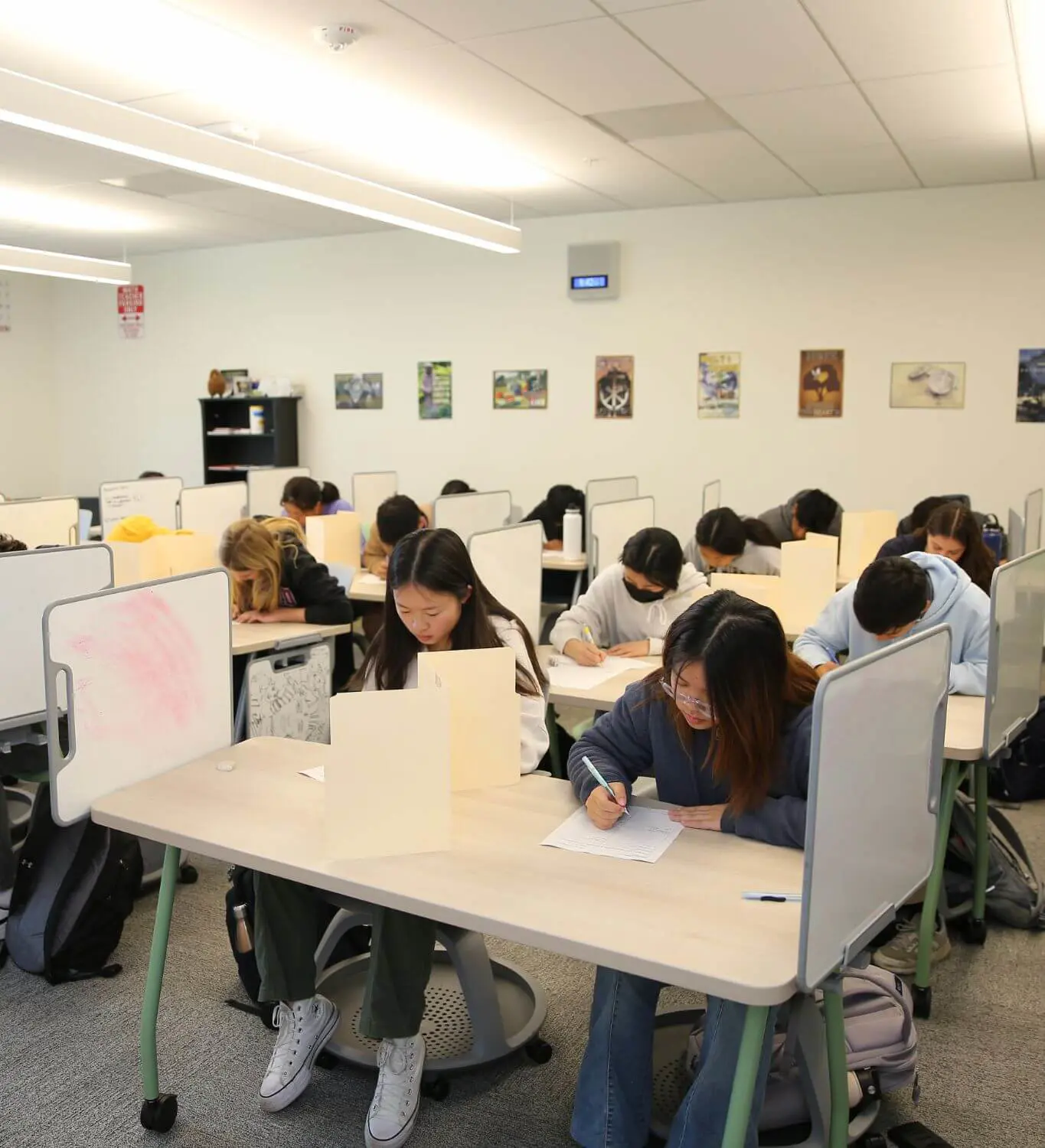 Class full of students sitting at desks with vertical dividers while taking tests.