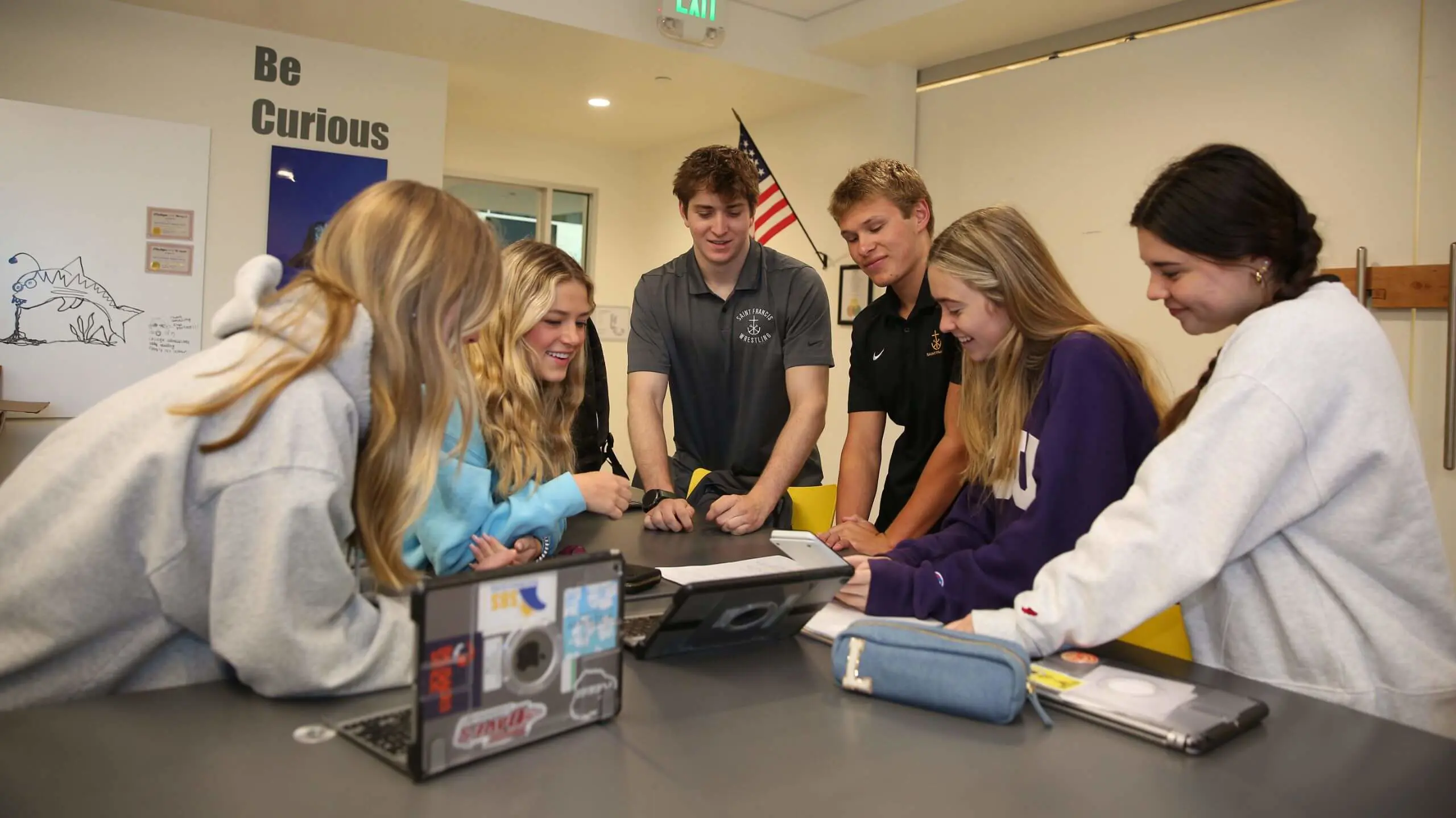 A group of six students gathered around a table working on a project together.