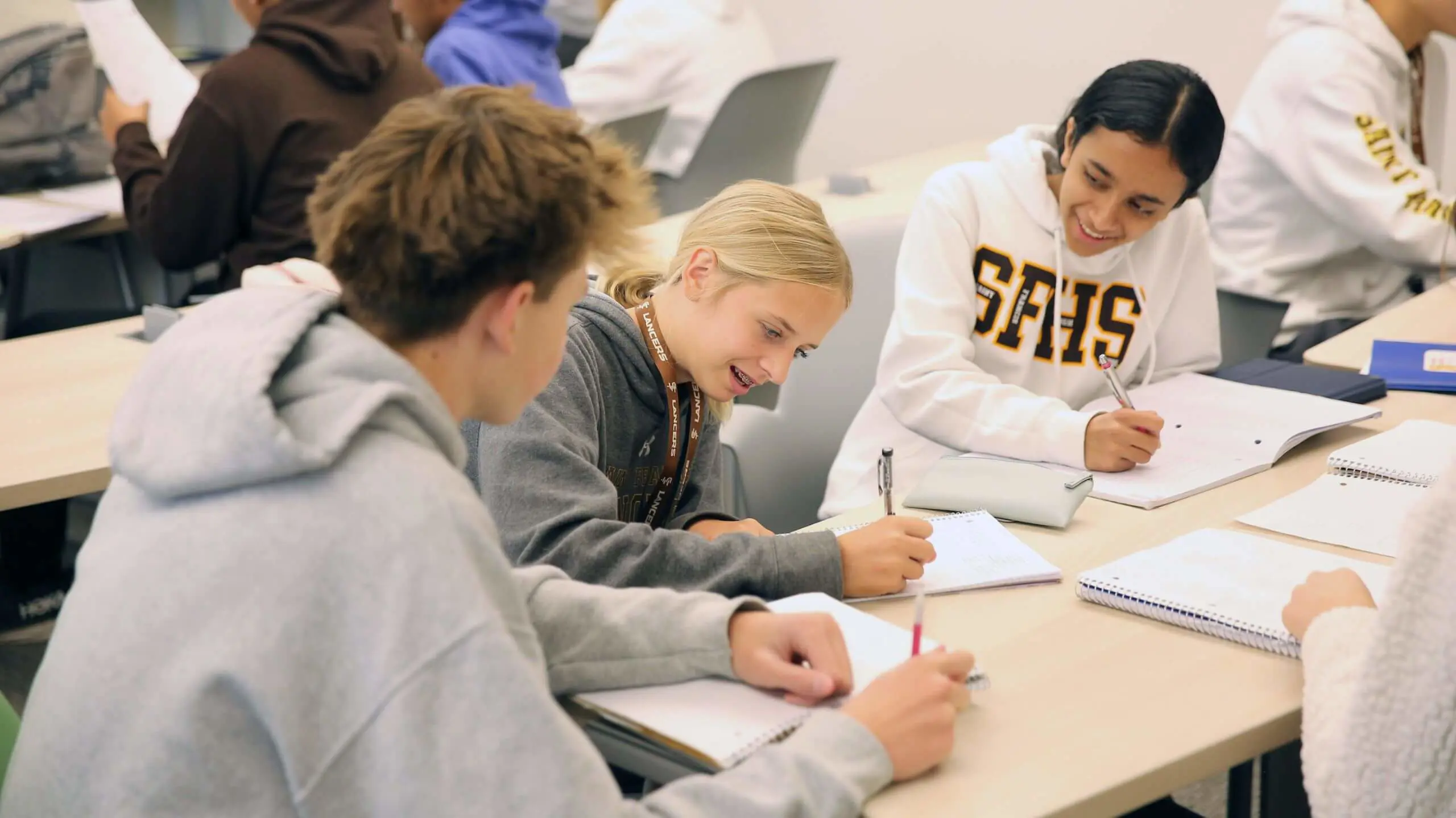 Three students sitting at a desk taking notes in a notebook.