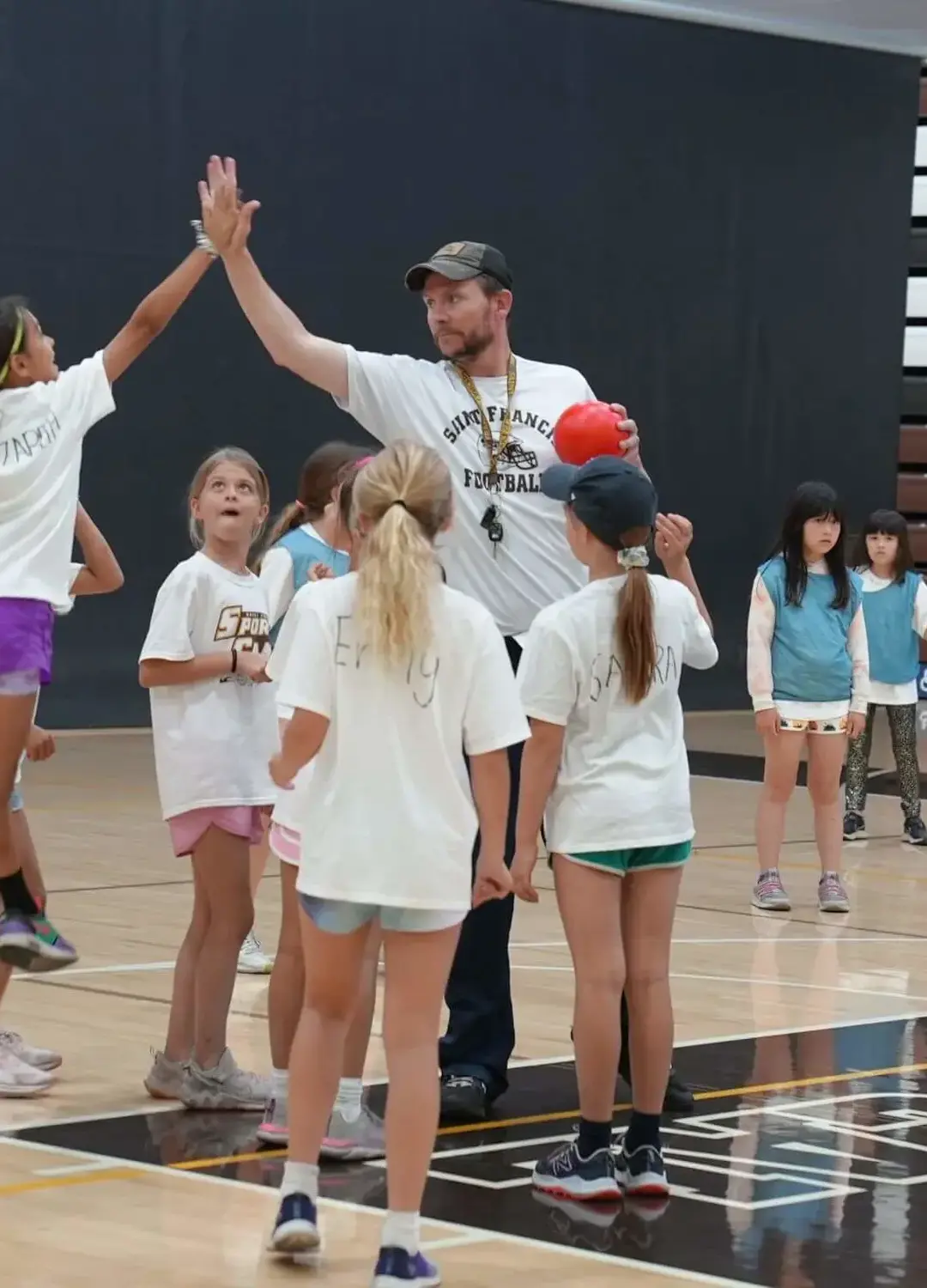 Counselor and camper high-fiving while playing handball in Burns gym.