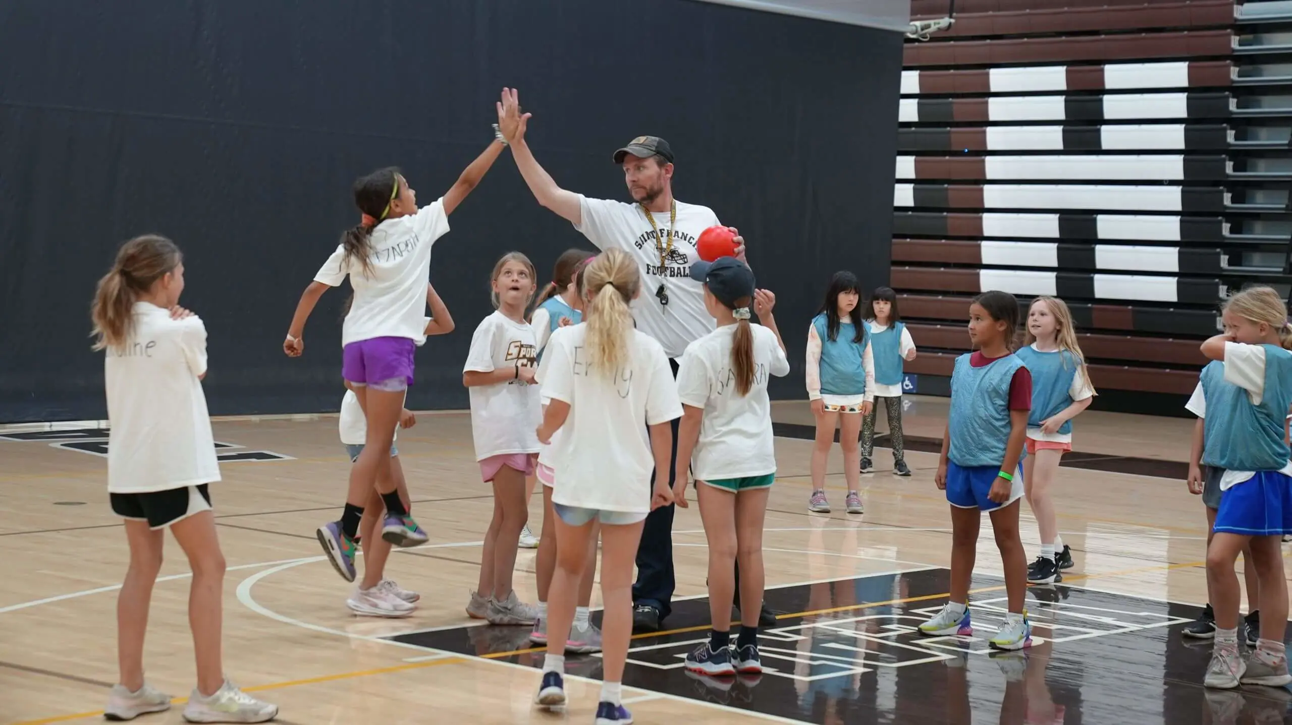 Counselor and camper high-fiving while playing handball in Burns gym.