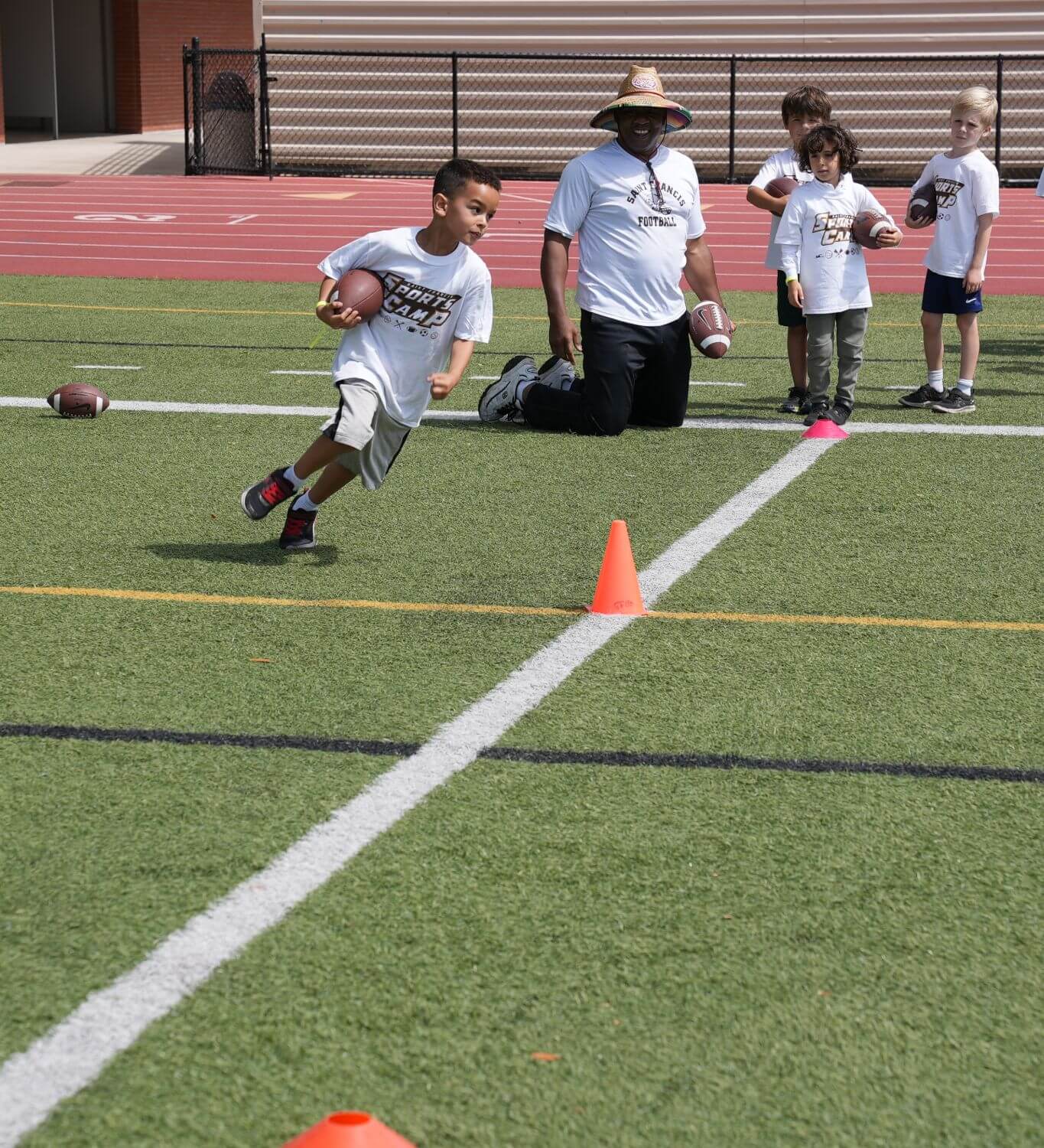 Camper with a football running a drill as the counselor watches on.
